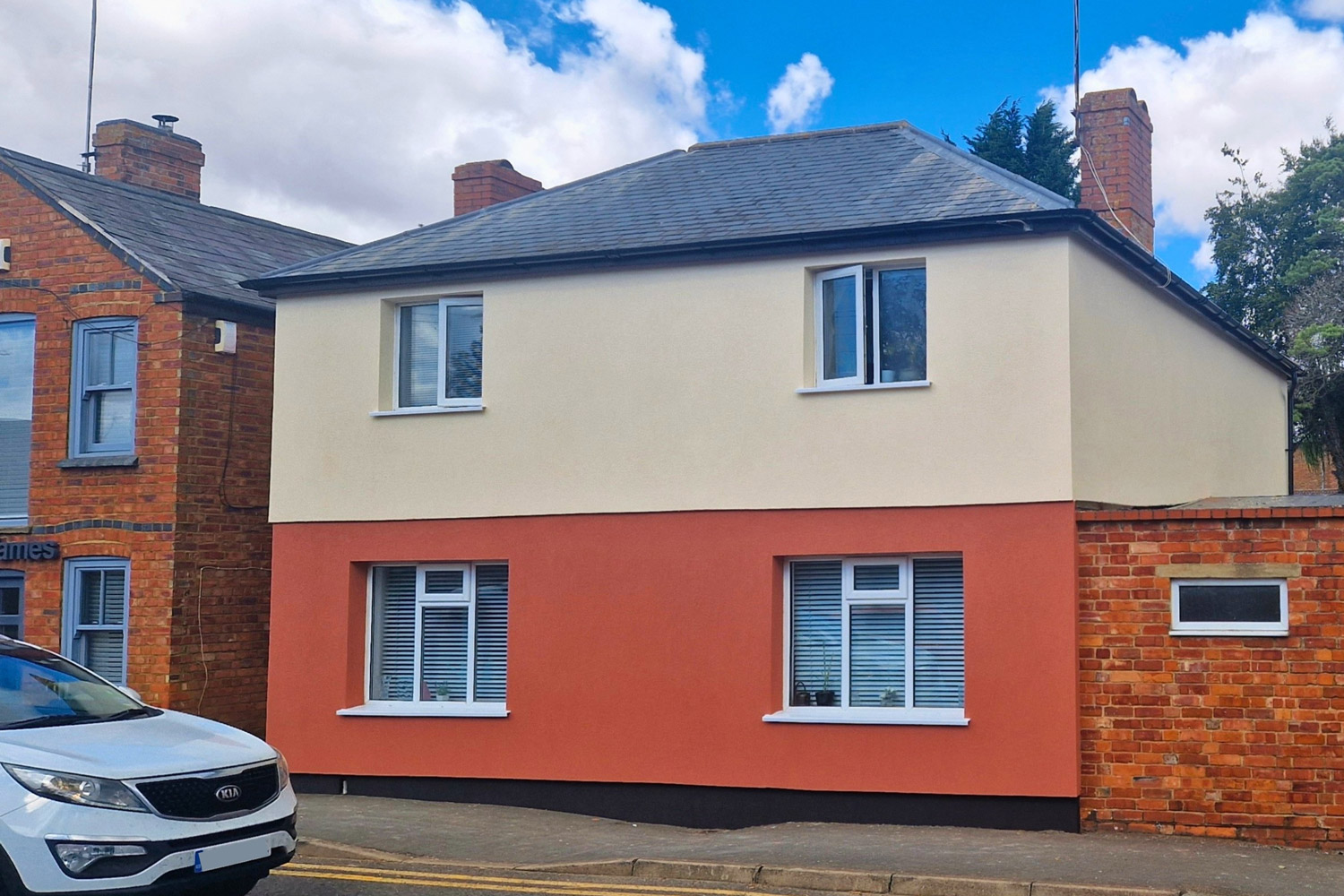 A beautifully rendered UK home featuring a distinct two-tone silicone finish, with a cream upper elevation and a striking terracotta red lower half.